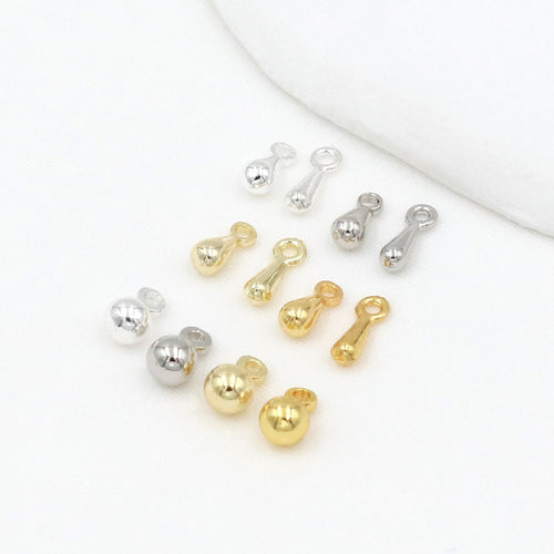 Gold-plated teardrop and ball charms in gold and silver tones arranged on a white surface