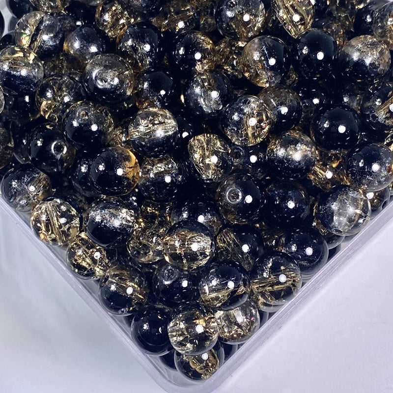 Close-up of black and gold crackle glass beads in a clear container on white