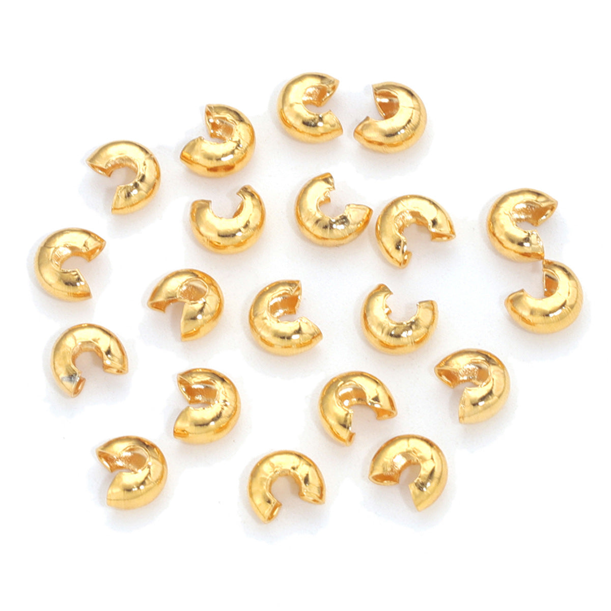 Group of small gold C-shaped crimp bead covers scattered on a white background.