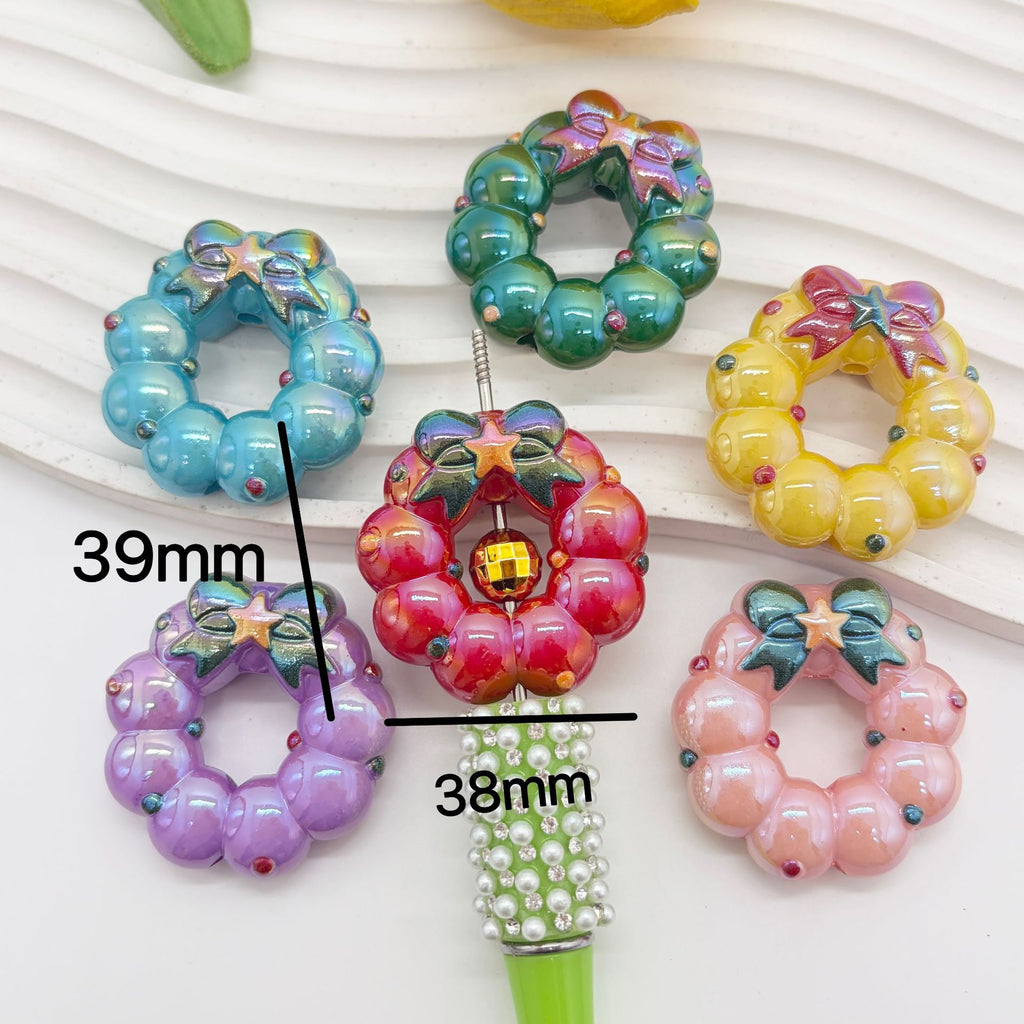 Six colorful wreath-shaped acrylic focal beads on a white ribbed surface with measurement lines