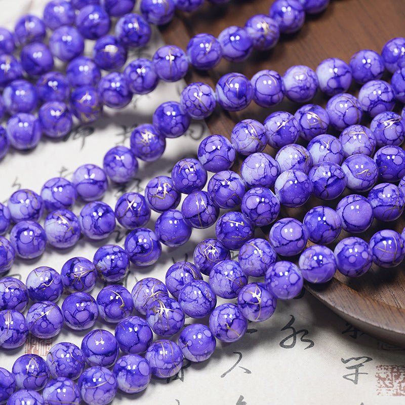 Purple marbled porcelain bead strands with gold veins on a light surface