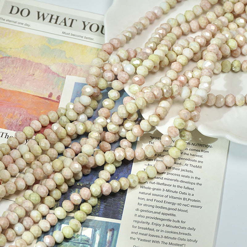 Multiple strands of pale pink, cream, and light green faceted porcelain beads on newspaper