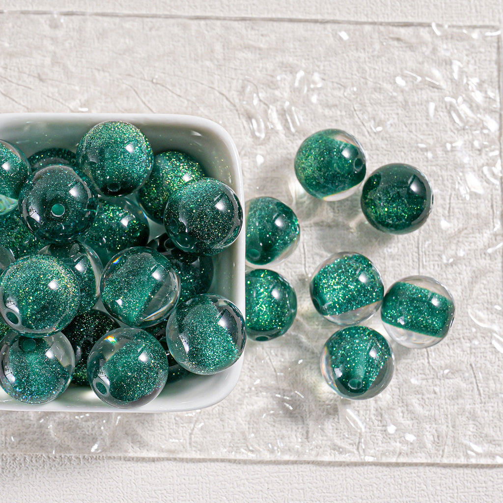 Green glitter round beads in a white dish and scattered on textured white surface