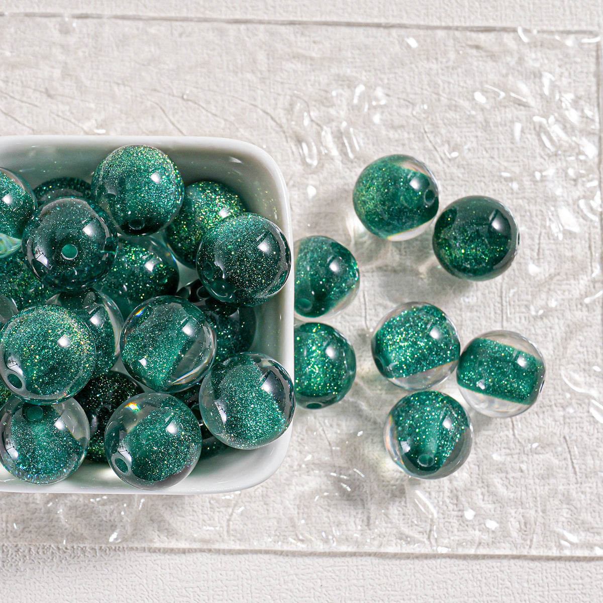 Green glitter round beads in a white dish and scattered on textured white surface