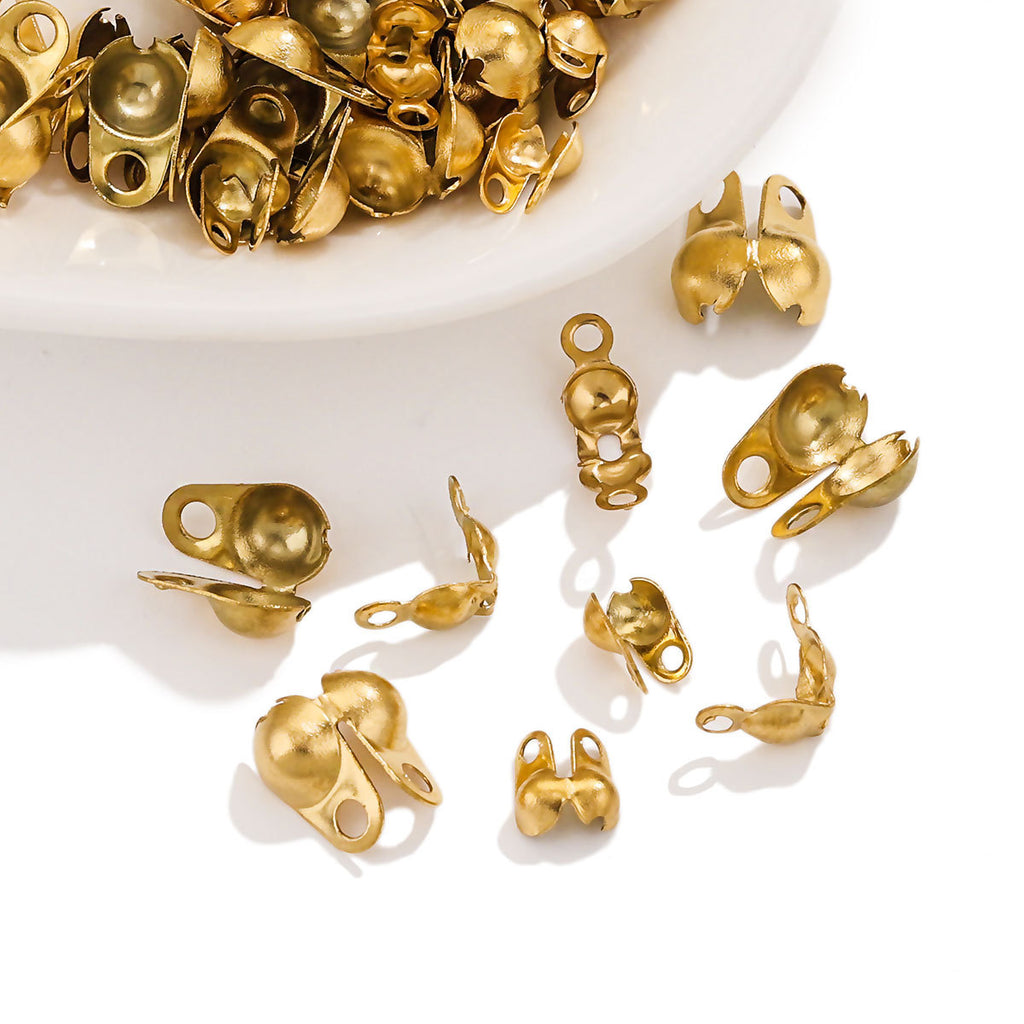 Small gold ball chain connector clasps scattered on a white surface, more piled in a white bowl