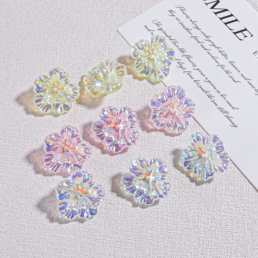 Nine iridescent holographic resin flower beads arranged on a textured white surface by a card