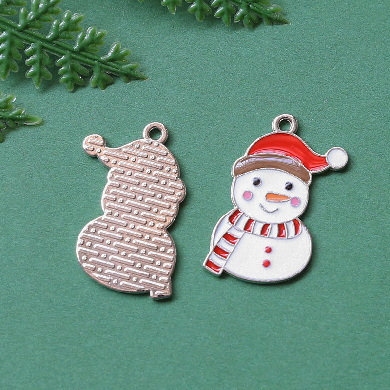Two Christmas-themed metal charms on textured green background, silver snowman