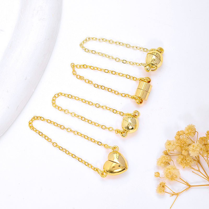 Four gold magnetic necklace clasps with safety chains in ball, cylinder, and heart shapes on white with dried flowers
