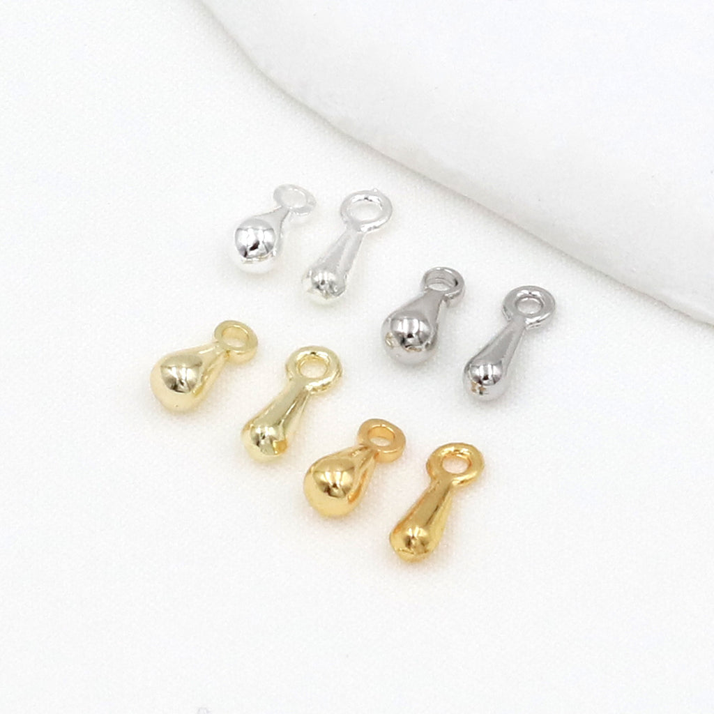 Eight gold and silver teardrop charms with loop ends arranged on a white fabric background