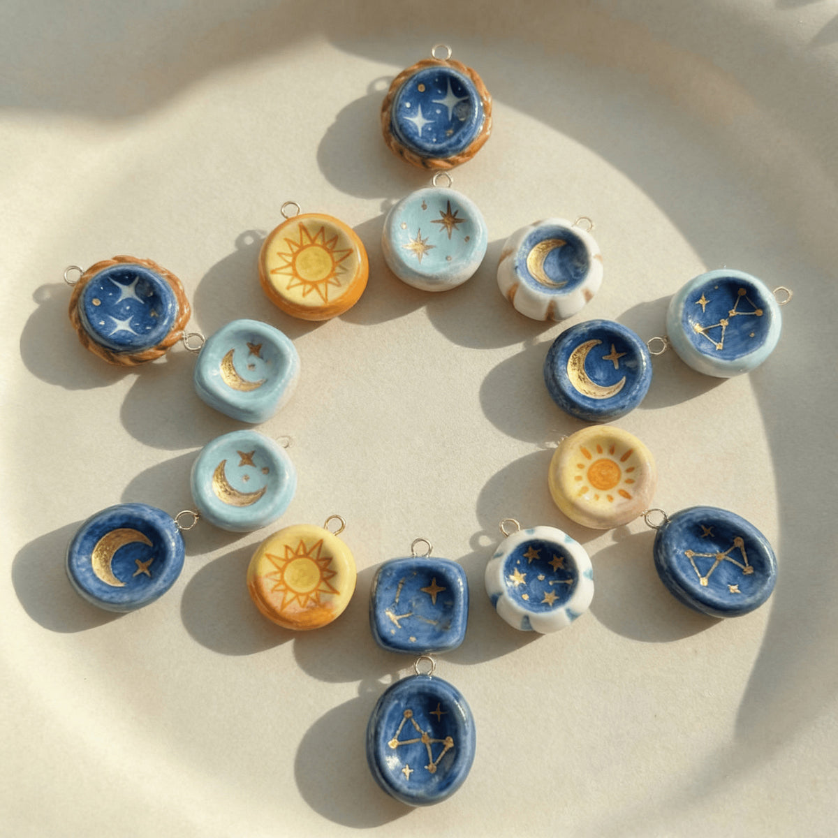 Sixteen small ceramic celestial charms in blue, yellow and white with sun, moon and star designs arranged in a circle.
