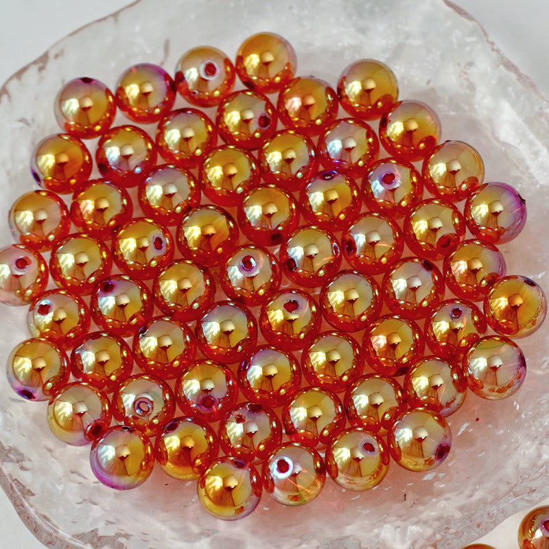 A pile of small iridescent glass beads with a metallic gold and orange finish, resting on a clear textured dish.