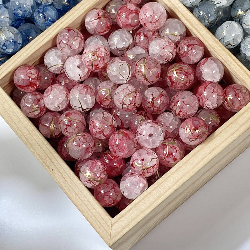 Pink and red crackle glass beads with gold-silk details in a wooden tray