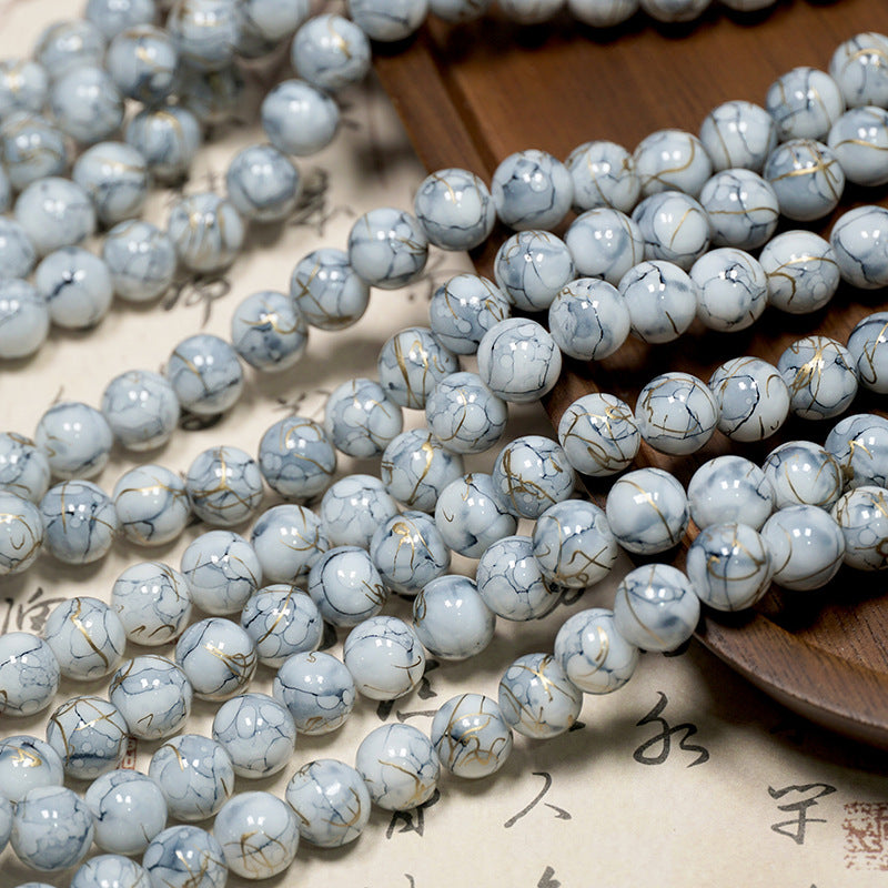 Close-up of white-gray marbled porcelain beads with gold inclusions draped over wood