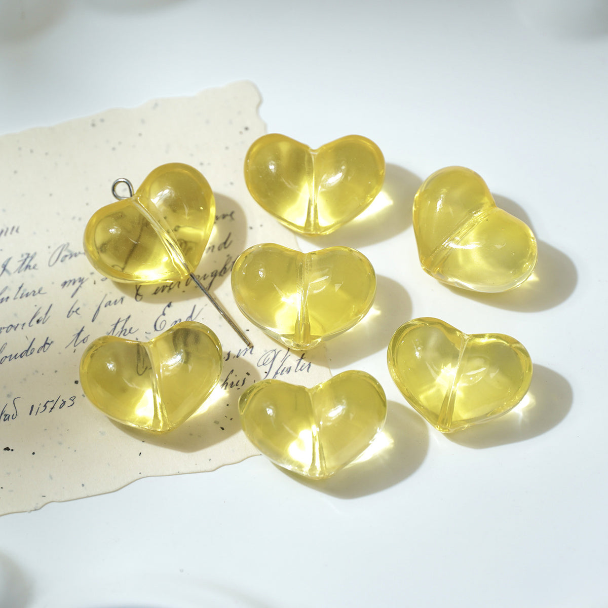 Six translucent yellow heart-shaped glass beads with silver jump rings on white