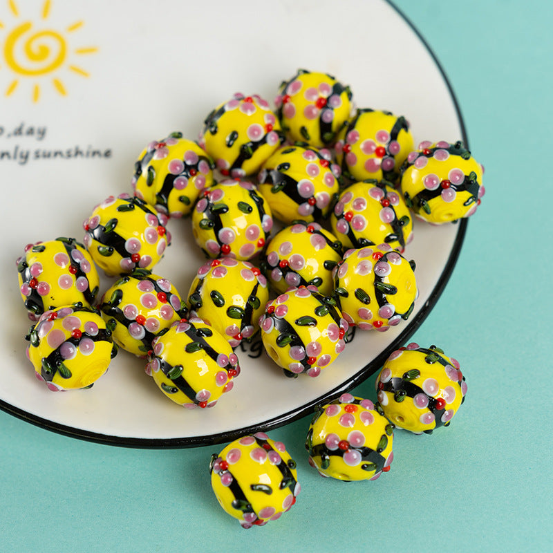 Yellow perforated glass round pendant beads with pink, black, and red details on a white plate