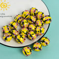 Yellow perforated glass round pendant beads with pink, black, and red details on a white plate