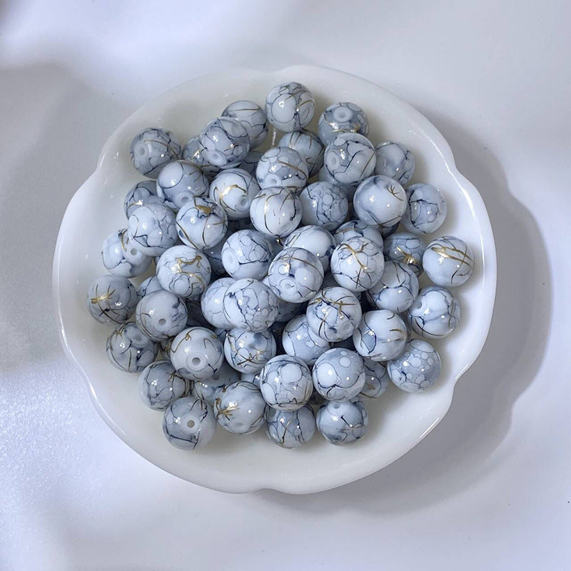 White bowl of marbled white glass beads with black and gold veining