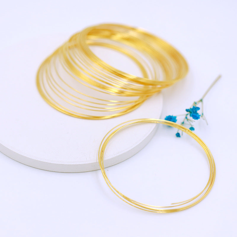 Coiled gold-plated memory wire bracelets on white round platform with blue flower