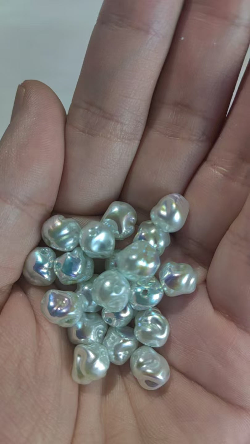 Close-up of a hand holding a pile of irregular white faux pearl beads with pearlescent sheen