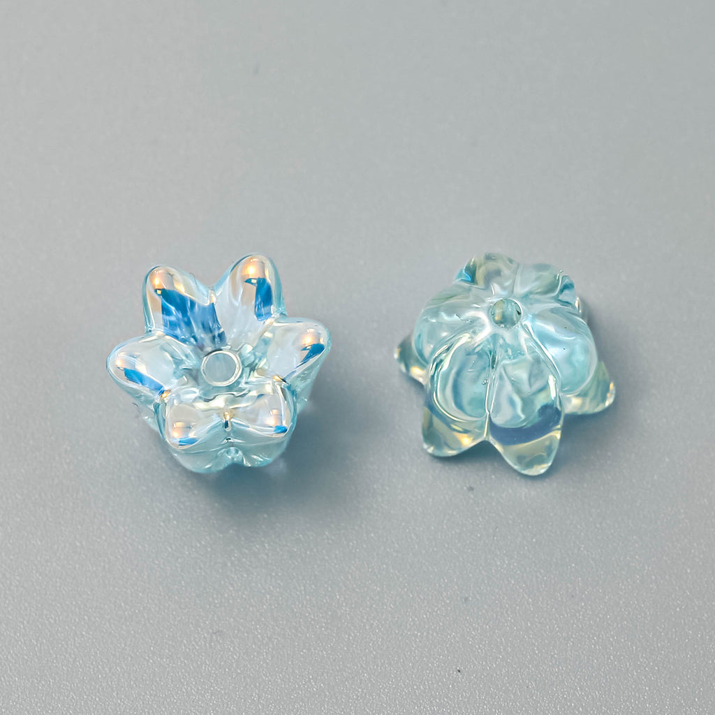 Two light blue iridescent lily-shaped beads, one showing front and one showing back, on a neutral gray background
