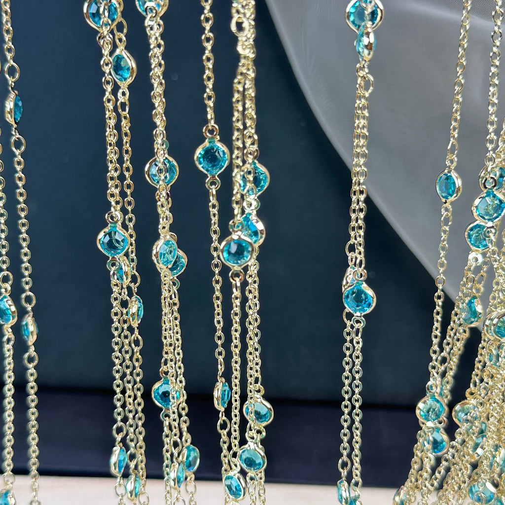 Gold-tone chain fringe necklace with faceted light blue gemstones on dark