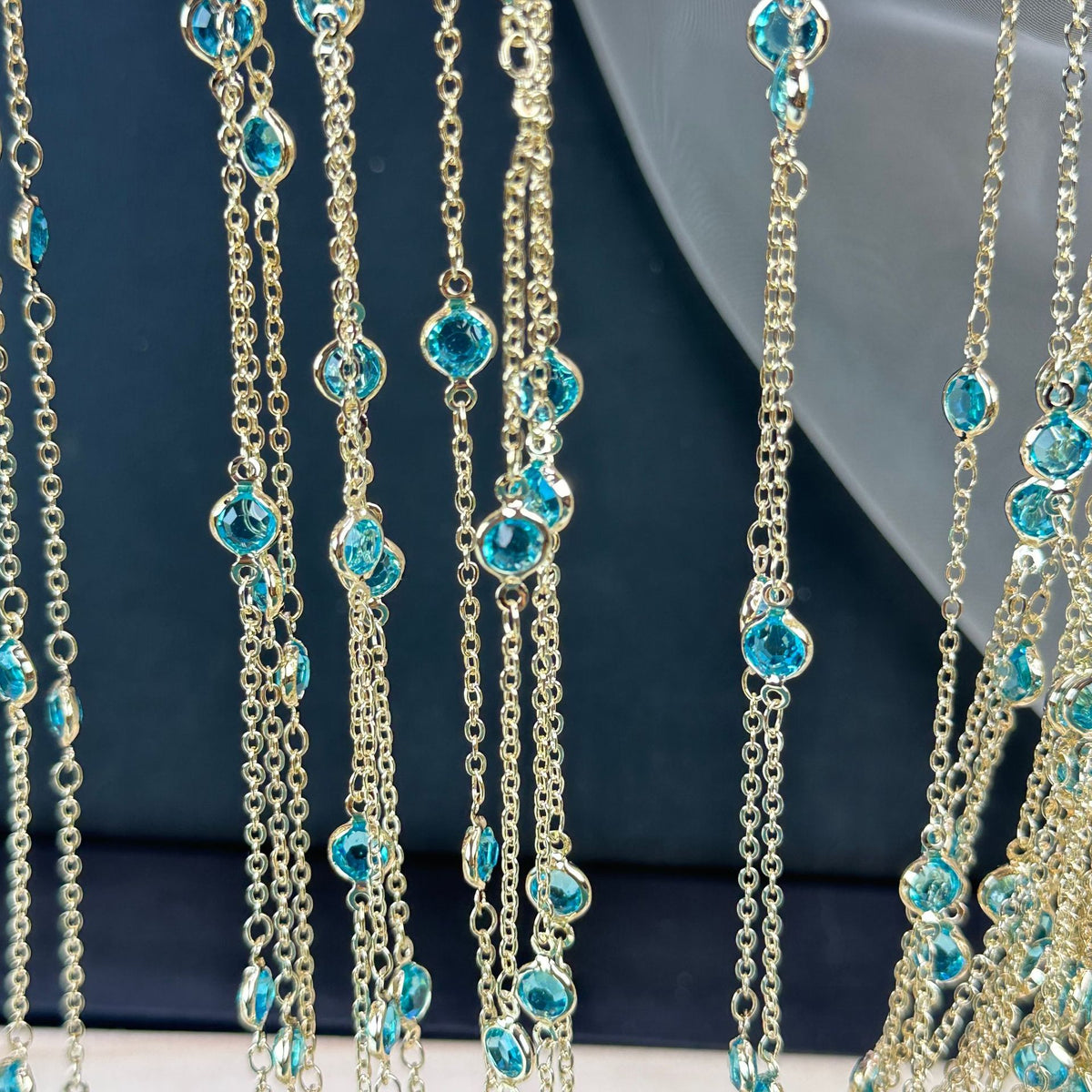 Gold-tone chain fringe necklace with faceted light blue gemstones on dark