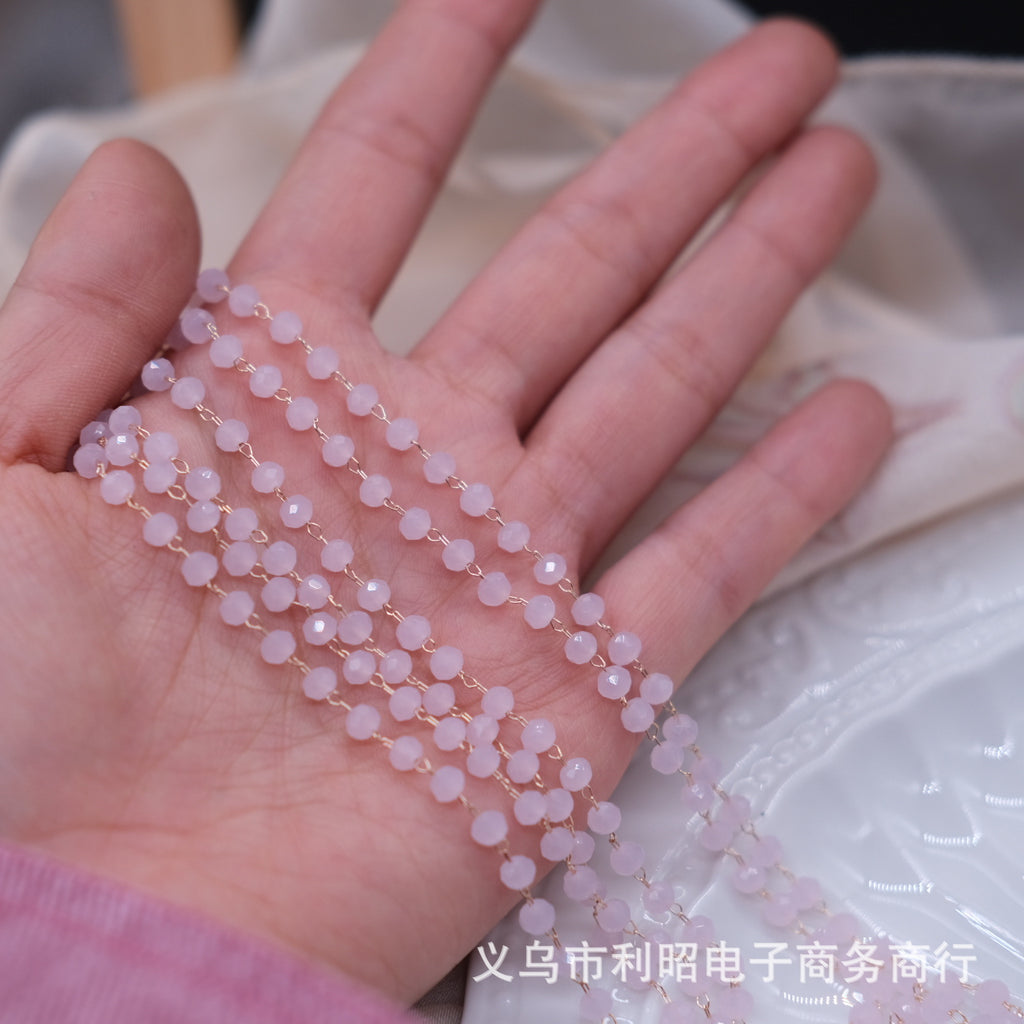 A close-up of a hand holding several strands of pale pink round beads with small gold links, photographed against a soft white fabric background.