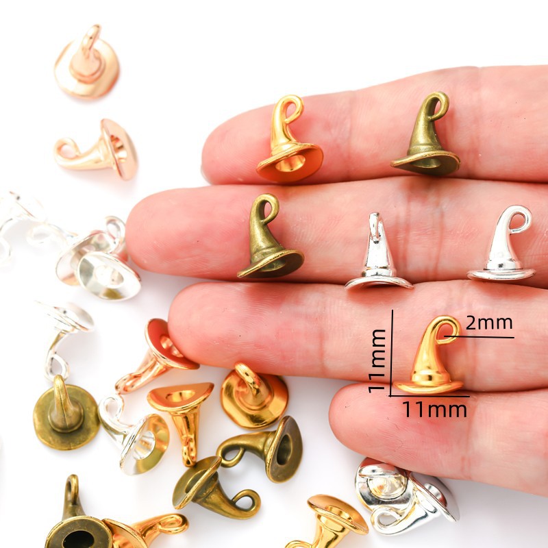 Small metal fairy hat charms in gold, bronze, silver, and clear plastic, displayed on a person's fingers with dimension labels showing 11mm height and 2mm width.