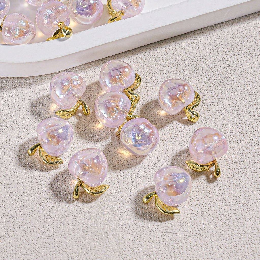 Several small pear-shaped iridescent mini peach beads with gold leaf accents on a textured beige surface