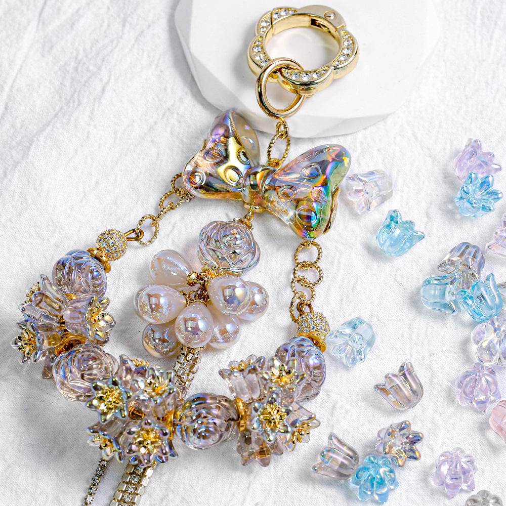 Gold-tone charm with iridescent butterfly bow, pearl-like and floral beads on white surface with scattered lily beads