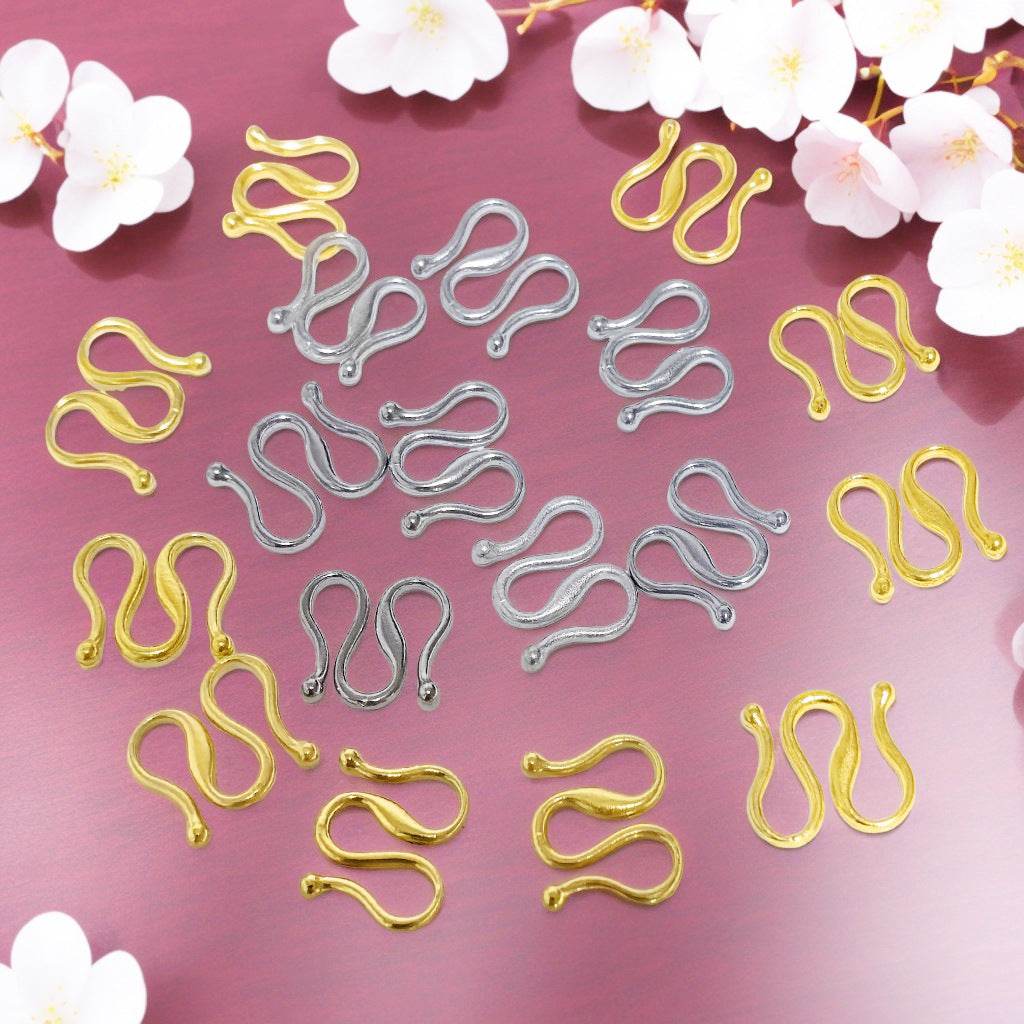 Gold and silver S-shaped hook clasps scattered on pink background with white cherry blossoms.