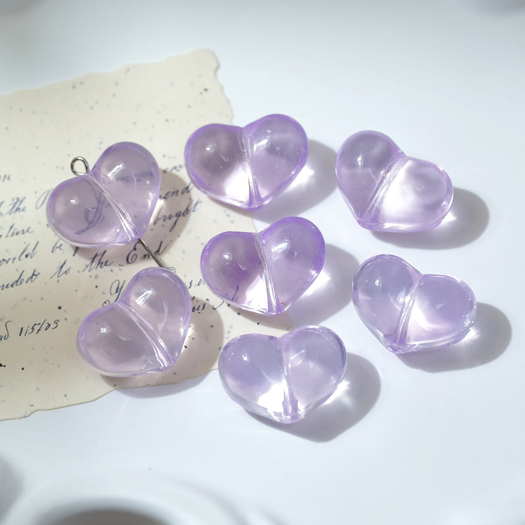 Seven translucent light purple heart-shaped glass beads with metal loops on white