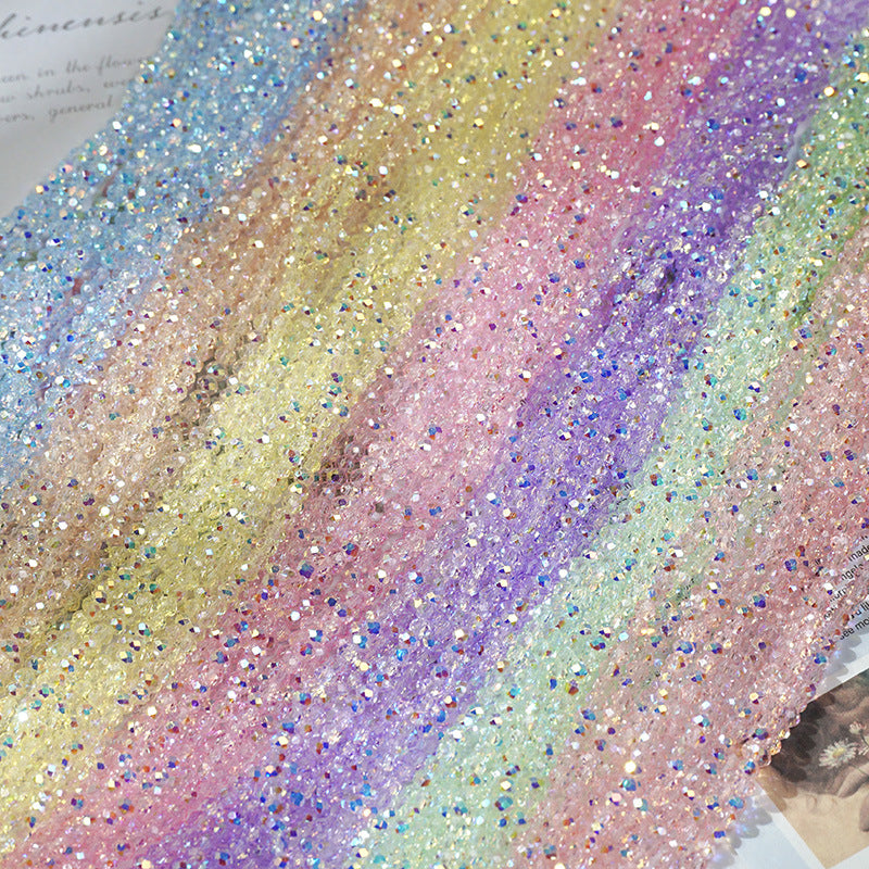 A close-up of iridescent sequin fabric arranged diagonally in pastel rainbow stripes, including blue, gold, yellow, pink, purple, green, and peach tones.