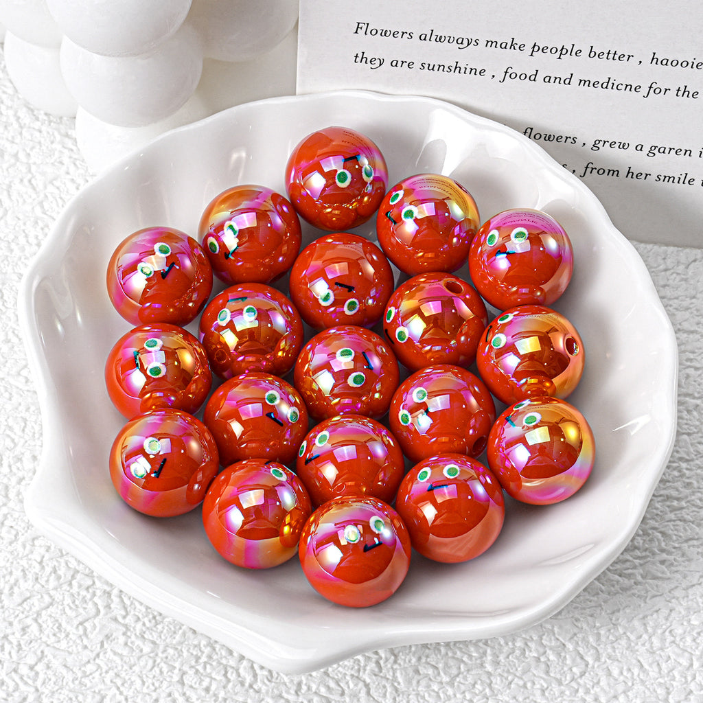 Glossy red-orange iridescent resin beads with cartoon faces in white ceramic dish on textured surface