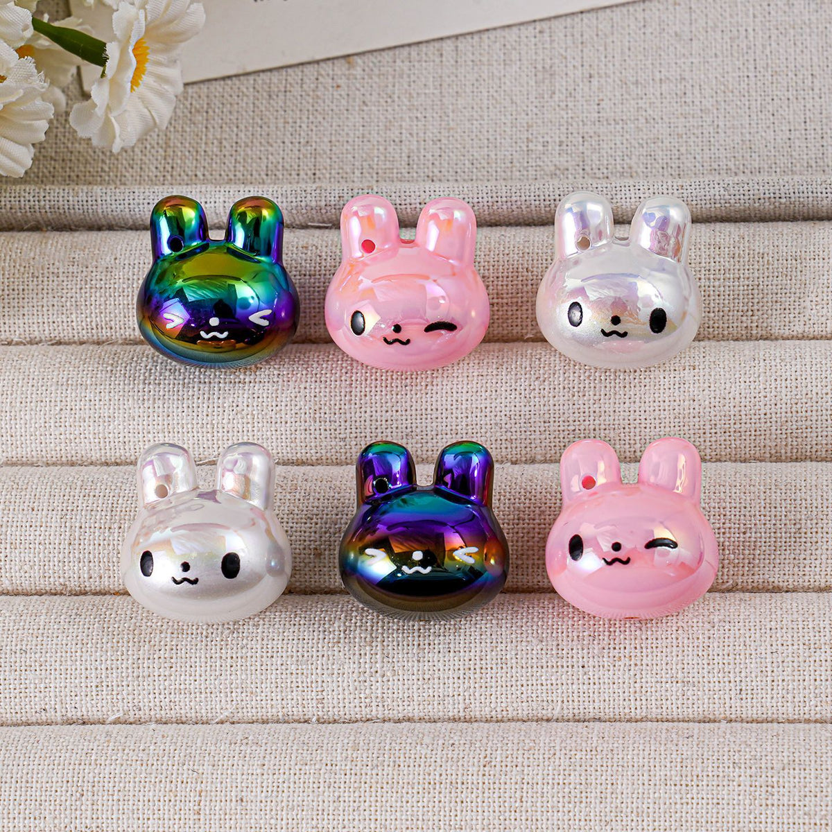 Six bunny-shaped acrylic charms in rainbow, pink and white on beige fabric surface