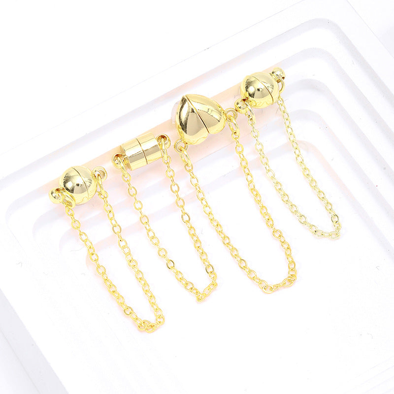 Four gold magnetic necklace clasps with safety chains in ball, cylinder, and heart shapes with long chains on a white tray