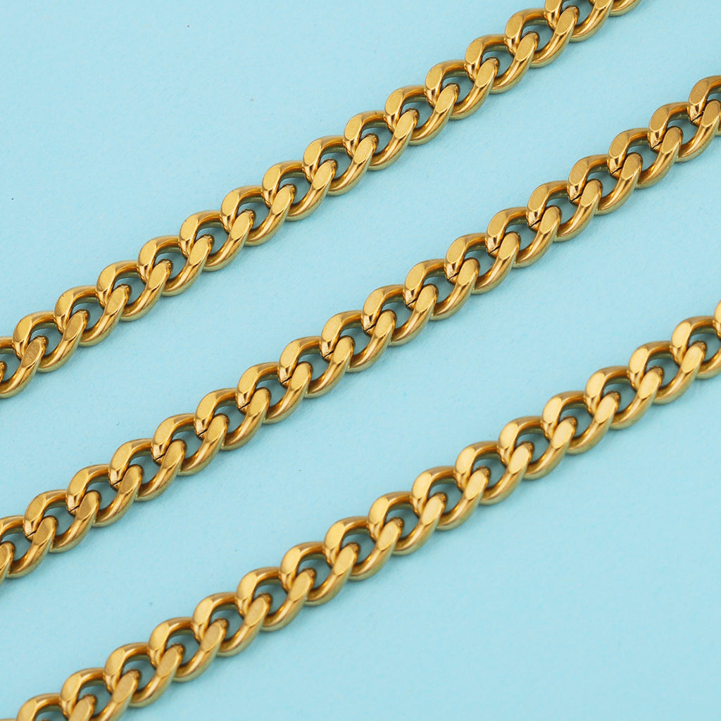 Three gold-plated NK Cuban curb chains laid diagonally on a light blue background