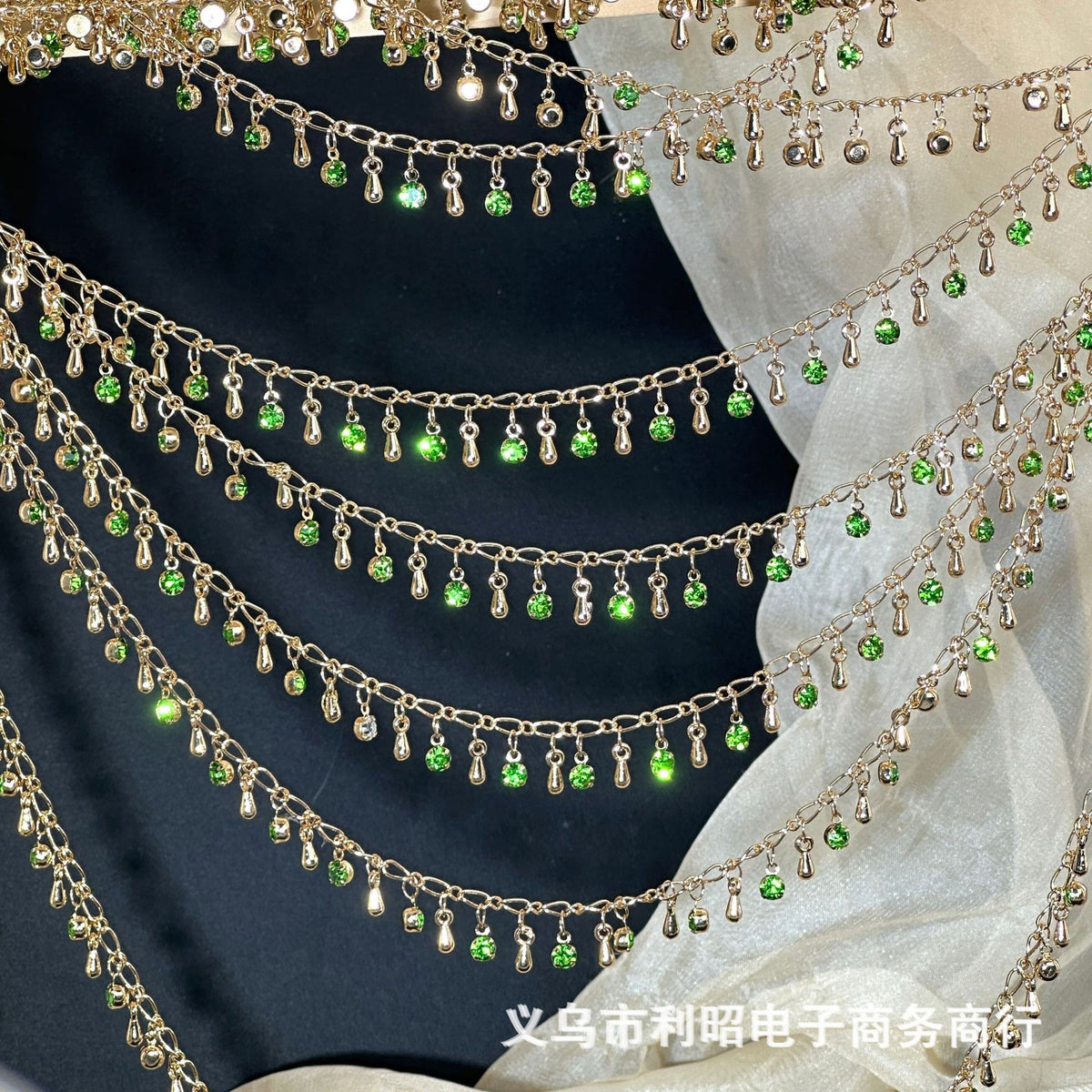 Gold chains with dangling green teardrop rhinestones draped over black and white fabric