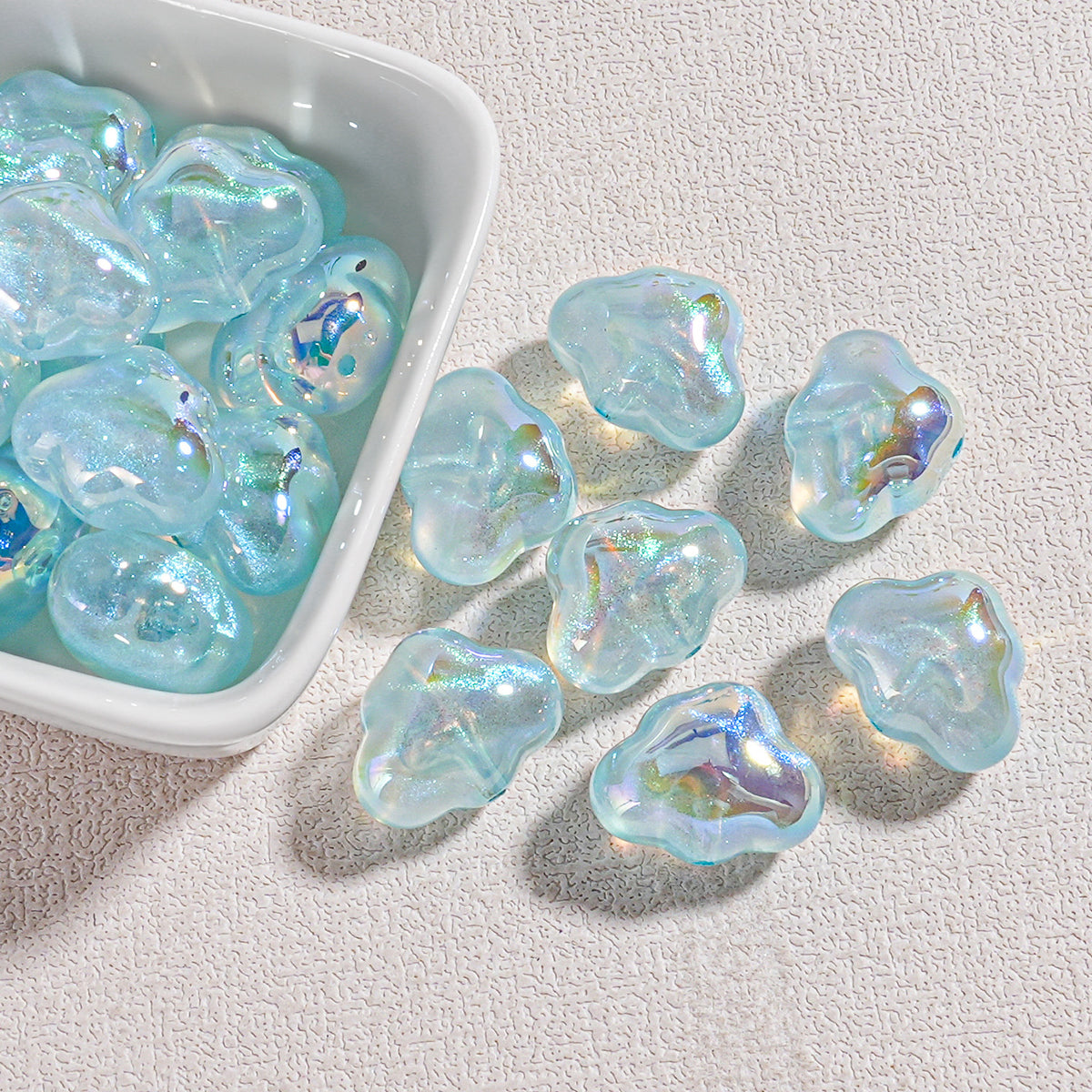 Iridescent light blue cloud-shaped resin beads with aurora shimmer in a white bowl and on a textured white surface