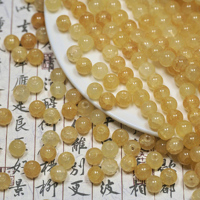 Yellow ice-crackle glass beads spilling from a white plate onto calligraphy paper