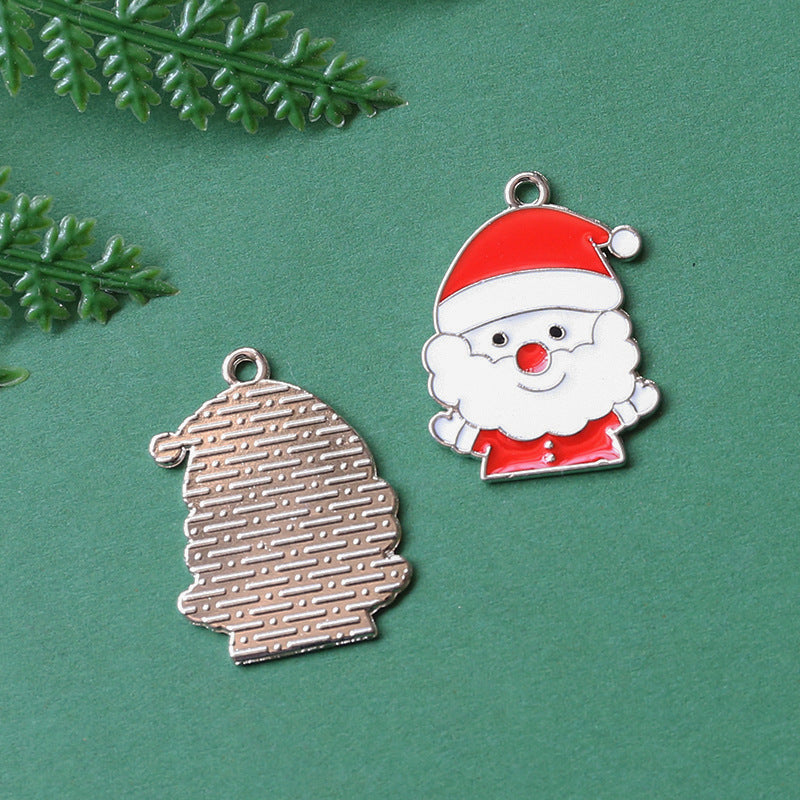 Two Christmas-themed metal charms on textured green background, Santa hat shaped