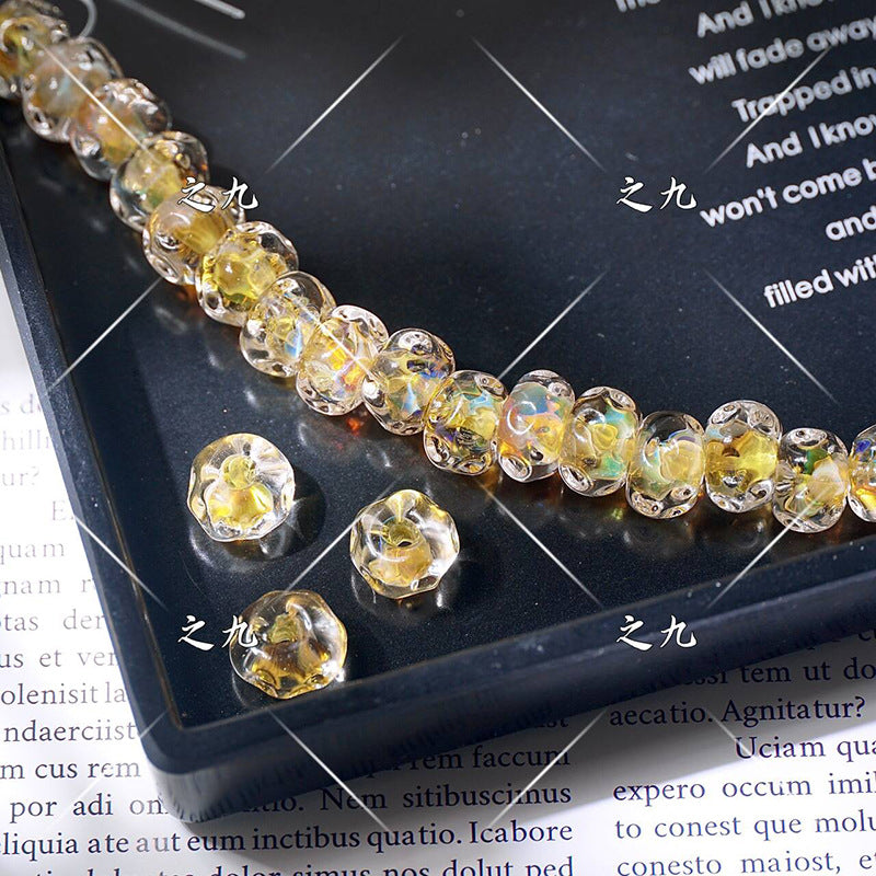 Faceted clear lampwork beads with yellow iridescent finish on a black tray, loose beads