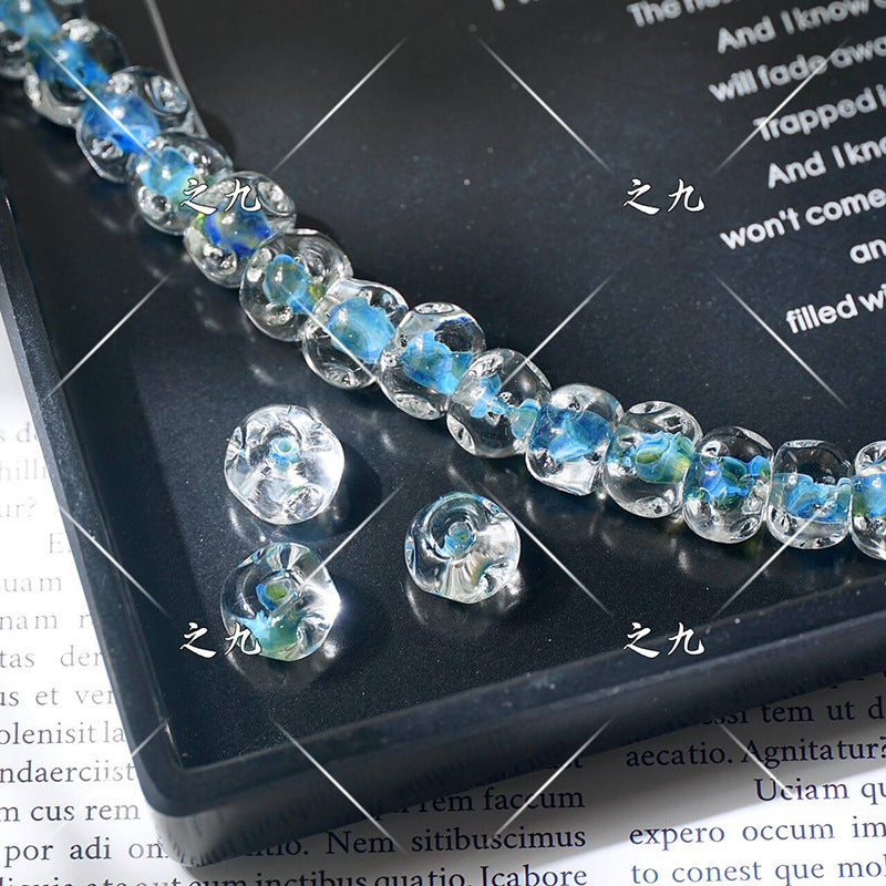Clear lampwork glass beads with blue-green centers on a black tray, loose beads in front