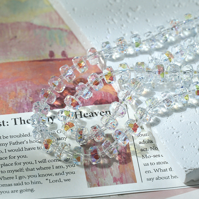 Clear faceted crystal beads with iridescent reflections arranged in strands over an open book on a textured surface
