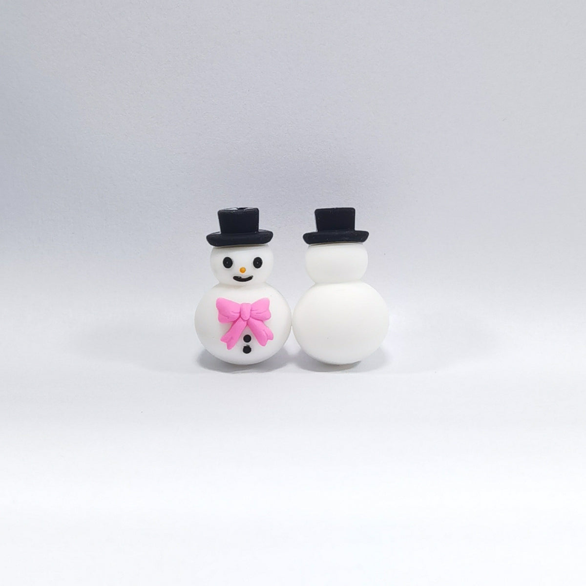 Two snowman silicone focal beads with black top hats, one facing forward with pink bow tie