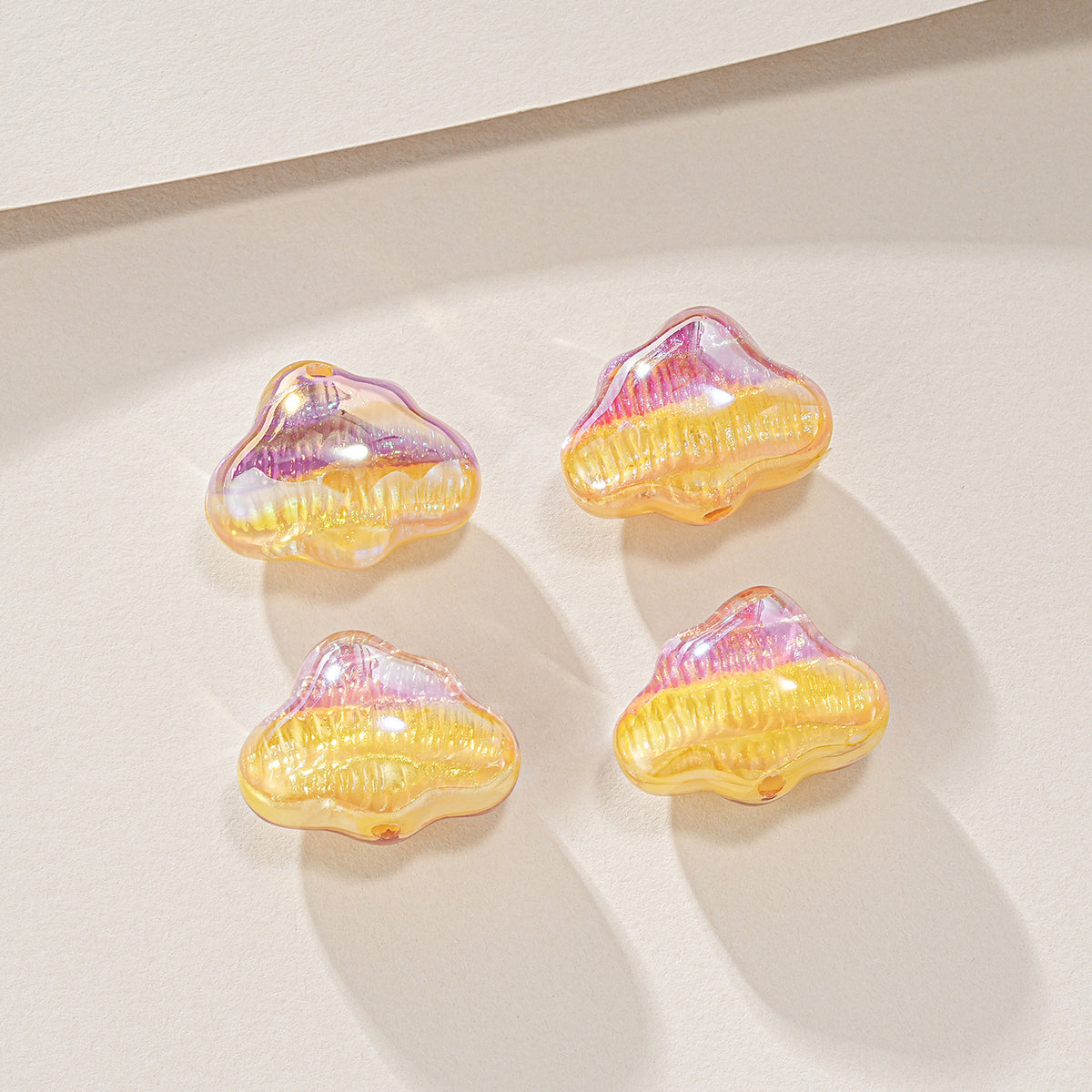 Four small cloud-shaped resin beads with a yellow and pink iridescent finish on a light beige background.