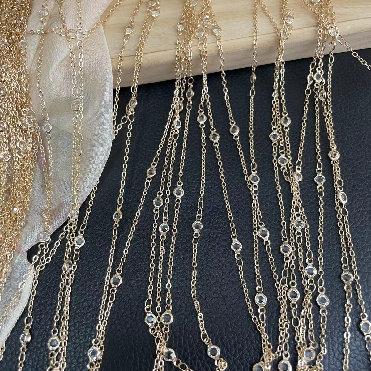 Gold chain fringe with clear rhinestone beads draped over light wood surface and black fabric