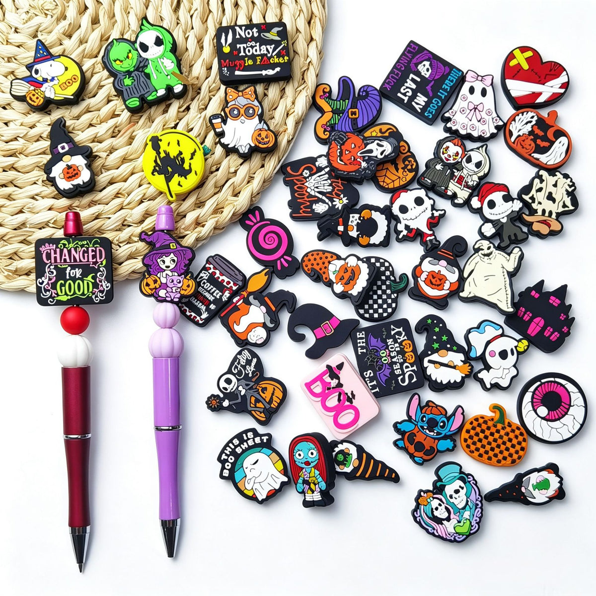 Flat lay of assorted Halloween silicone charms with pumpkins, ghosts, skulls, and witches beside two pens and a woven straw hat