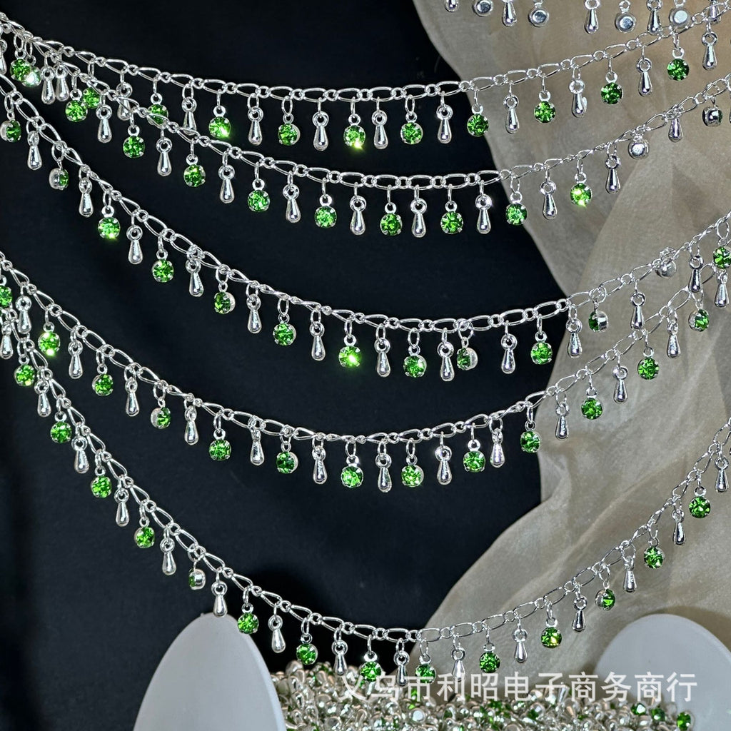 Silver chain with hanging green rhinestones and teardrop charms on black and beige fabric