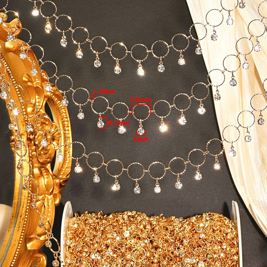 Gold-toned beaded garland with circular rings and dangling clear crystal drops, shown laid out on a dark surface with decorative props. Red text labels indicate bead diameters: 1.